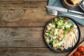 Delicious Caesar salad in bowl on wooden table, flat lay. Space for text