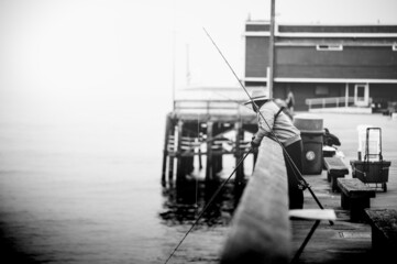Grayscale shot of a fisherman standing on a pier with a rod