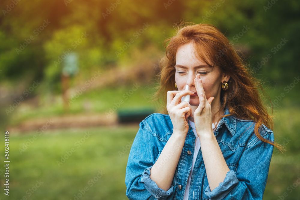 Wall mural Nasal Spray, Female hand spraying nasal spray with blurred background. Woman Using Nose Spray. Young Woman is Having Sinusitis Problems Outside in Nature.