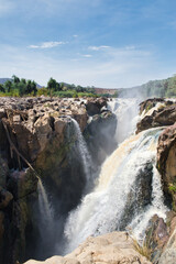 Portrait shot of Epupa waterfalls in northern Namibia at the border to angola showing the mast amounts of water falling down the cliffs with short exposure to freeze the action in time.  - obrazy, fototapety, plakaty