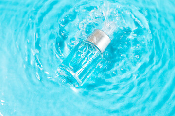 Bottle serum or cosmetic oil in clean transparent water with sunlight on blue background, flat lay, top view, copy space. Cosmetic spa medical skin care concept.