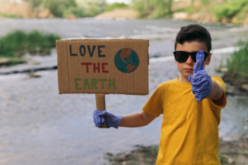 A serious young boy wearing a yellow t-shirt and blue gloves holding a cardboard sign drawn by hand...