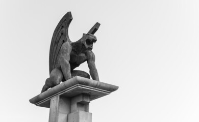 Low angle grayscale shot of a Gargoyle statue under a cloudy sky