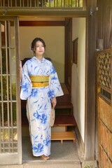 日本家屋の玄関先でポーズをとる浴衣姿の若く美しい女性