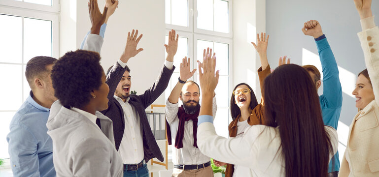 Overjoyed business team cheering, celebrating good sales result, and financial goal achieving. Joyful contented colleagues laugh celebrating success and raise their hands for emotional high fives.
