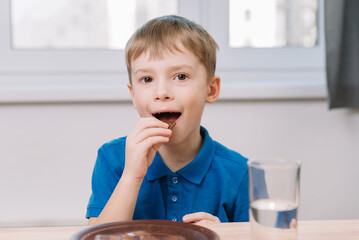 The boy eats chocolate, sits at the kitchen table at home. Baby food concept.