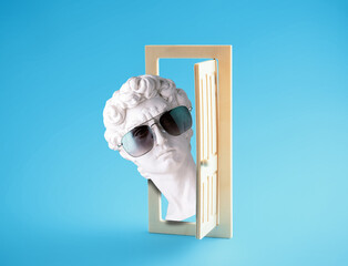 David's head in sunglasses looks out of  wooden door on  blue background. Summer poster.