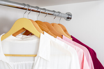 Close-up of women's blouses hanging on hangers from white to dark pink gradient.