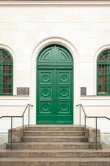 Beautiful exterior of a traditional green wooden door with stairs and green arch metal windows