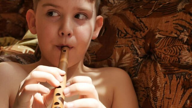 portrait caucasoid teenager boy playing the armenian wind instrument sring. the child blows air into the national pipe made of wood. Copy space, slow motion