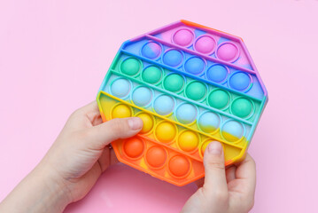 popular toy multi-colored pop it in the form of an octahedron in the hands of a child on a pink background