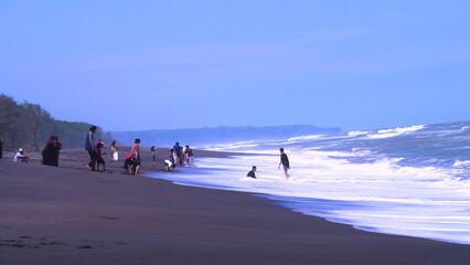 Yogyakarta, Indonesia - may 4 2022 : On a beautiful beach with quite big waves some people are playing, They are quite careful and keep their distance so as not to be dragged by the waves