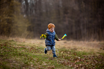 A little boy runs in the park with the flag of Ukraine and holds a bouquet