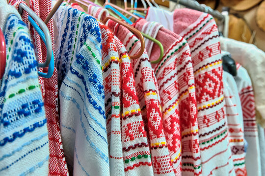 Traditional Russian national bright ornaments on woven dresses hanging on hangers.