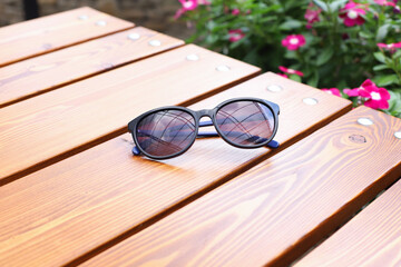 Fototapeta na wymiar Sunglasses on wooden glossy boards brown table. Summer outdoor cafe. Copy space.