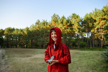 A boy in a red windbreaker against the backdrop of a forest with a compass in his hand.