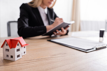 cropped view of notary writing near house model on blurred foreground.