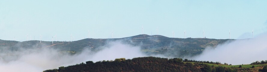 Fototapeta na wymiar Aerogeneradores situados en lo alto de unas colinas. Aerogeneradores entre la niebla matutina en el pueblo de El Granado en Huelva, Andalucía, España.