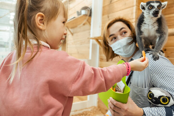 Portrait of young caucasian woman and her little daughter smiling while feeding lemur in zoo. Kid in the zoo © alexanderon