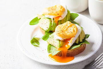 Eggs benedict on bun with spinach, avocado and hollandaise sauce. Delicious vegetarian breakfast concept.
