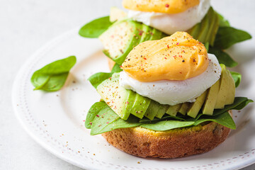 Eggs benedict on bun with spinach, avocado and hollandaise sauce. Delicious vegetarian breakfast concept.