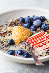 Quinoa porridge with apple, blueberry, peanut butter and hemp seeds for breakfast. Vegan food concept.
