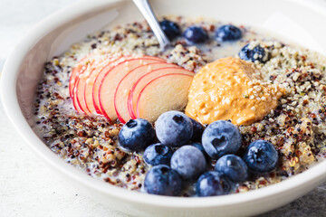 Quinoa porridge with apple, blueberry, peanut butter and hemp seeds for breakfast. Vegan food concept.
