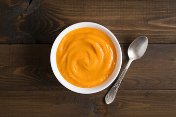 Pumpkin puree in a white plate on a rustic wooden table. Baby food. Top view.