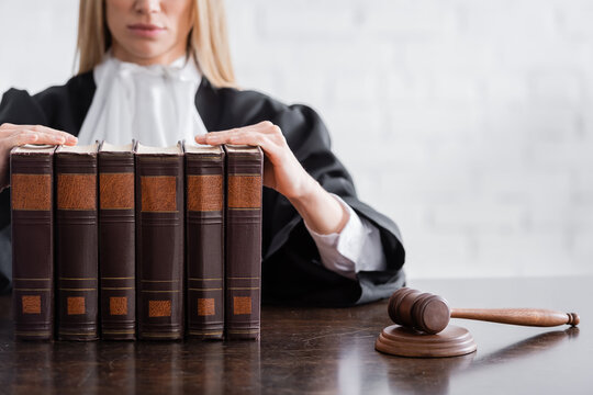 partial view of prosecutor sitting near collection of books and wooden gavel on desk.
