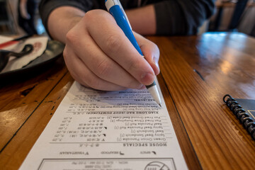 Close up, selective focus on a Caucasian man holding a pen, placing his order at a dumpling restaurant