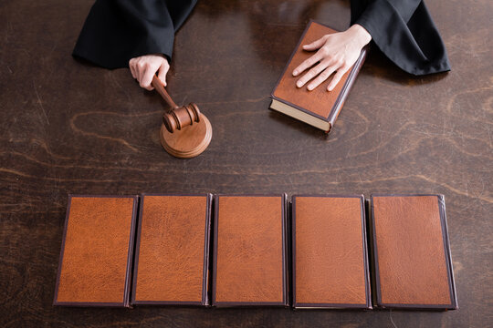 top view of cropped judge holding wooden gavel near collection of books.