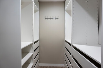 View of tall, white cabinets and drawers inside a narrow walk in closet inside a master bedroom