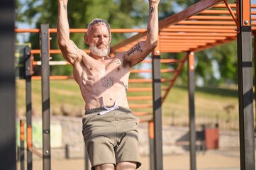 Obraz premium A gray-haired mature man having a workout on the open sports ground