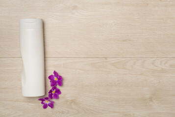 Body cream with flowers on wooden background, top view