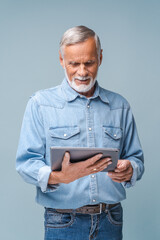 Cheerful mature man holding digital tablet isolated on blue, using tablet computer for remote work, reading electronic book, watching movies, web surfing