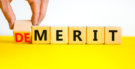 Demerit or merit symbol. Businessman turns wooden cubes and changes the concept word Demerit to Merit. Beautiful yellow table white background. Business and demerit or merit concept. Copy space.