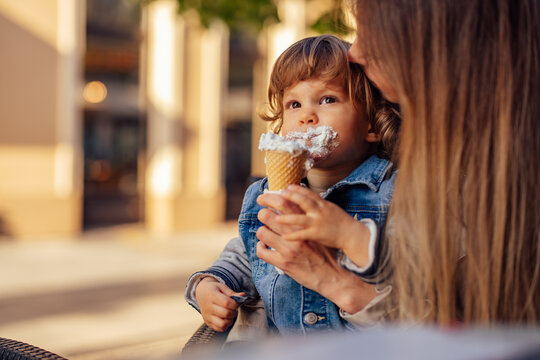 Cute male toddler, sitting on the mom's lap, eating ice cream.