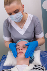 A female cosmetologist manually treats the patient's skin with a moisturizing and toning gel.