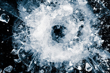 Hole in the ice, a breakthrough on black background. Shards of crushed ice spread away. The explosion of ice. Ice with cracks.