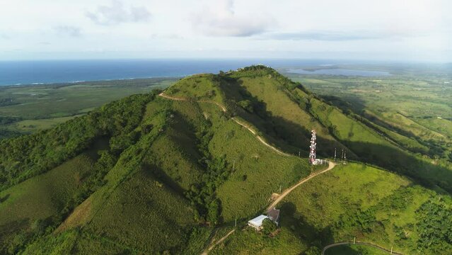 Summer igneous landscape against the background of the sea. Sunlight on green mountain slopes. Forest trees on meadow grass. Mountain tropical coast. Wildlife of the Dominican Republic.