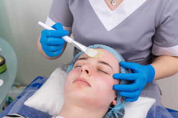 Naklejka premium Cosmetologist applies alginate mask with spatula on face of woman.