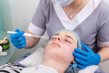 Fototapeta premium Cosmetologist applies alginate mask with spatula on face of woman.