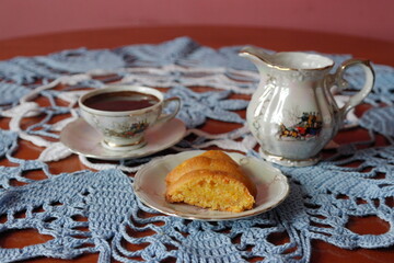 a porcelain cup with coffee and a piece of cake on an openwork tablecloth