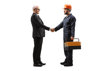 Full length profile shot of a worker in a uniform with a tool box shaking hands with a mature businessman