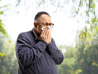 Mature man blowing nose with a paper tissue in a park