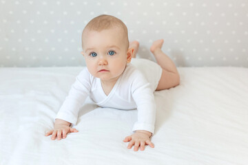 Cute toddler baby girl lies on bed at home and looking at the camera with smile