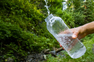 Close-up of woman hand taking pure water to bottle from mountain stream during trekking in...
