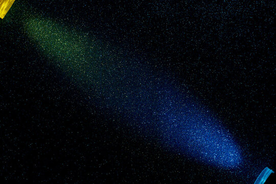 On a dark blue background, light green and light blue rays of light have merged into small multi-colored grains