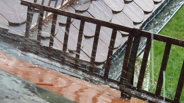 Close-up of a brown roof with snow guards and a gutter during a heavy thunderstorm with some hail falling down in springtime. Seen in Germany in May.