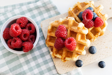 Belgian waffles with fresh berries and cup on wooden cutting board.